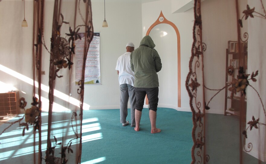 Men praying in the direction of of Mecca, taken from the women's side. The men's and women's prayer areas are separated by a lace curtain.