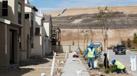 Workers plant vegetation outside new homes in the Otay Ranch Village of Escaya, which is bordered by the Otay Landfill shown here