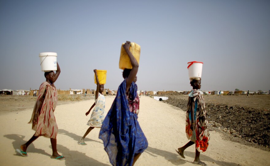 Women carry buckets and pails of water from a distribution site at the U.N. Protection of Civilians site. Severe water shortages at times force women and girls to fetch water from taps nearly a mile away.