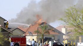 Firefighters stand on the roof of a neighboring house to put out flames from a house that caught fire after debris from a Harrier jet crashed into the ground in the area on June 4 in Imperial.