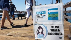 A sign warns people to practice social distancing and to wear a mask at the Imperial Beach pier, Sept. 14, 2020. 