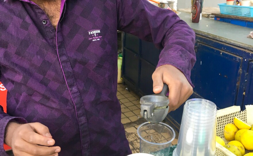 A soda vendor in Mumbai squeezes fresh lemons for a nimbu soda. The plastic jars in front of him contain spice mixes for different flavors.