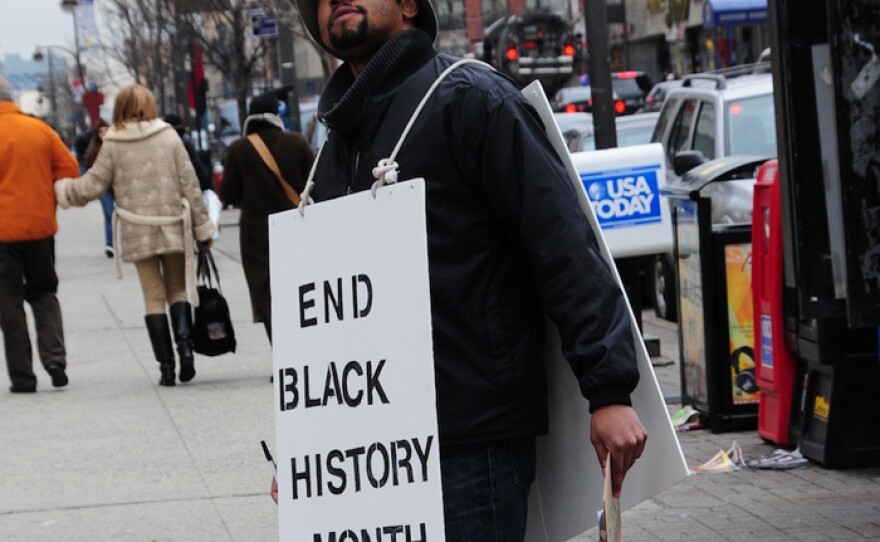 Filmmaker Shukree Tilghman wearing protest sign that reads "End Black History Month" in Harlem.