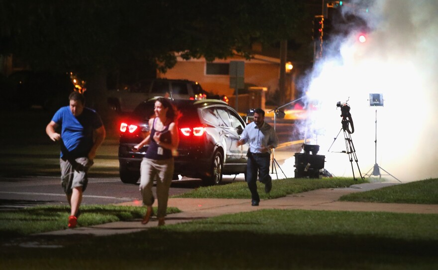 An Al Jazeera television crew, covering demonstrators protesting the shooting death of teenager Michael Brown, scramble for cover as police fire tear gas into their reporting position.