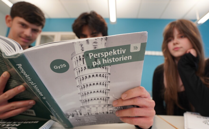 High school students from left, Vasilije Stjepanovic, Aslan Ozhan Kilicasan and Melina Sallahi pose with a history text book at Malmo Borgarskola high school in Malmo, Sweden, May 21, 2026.