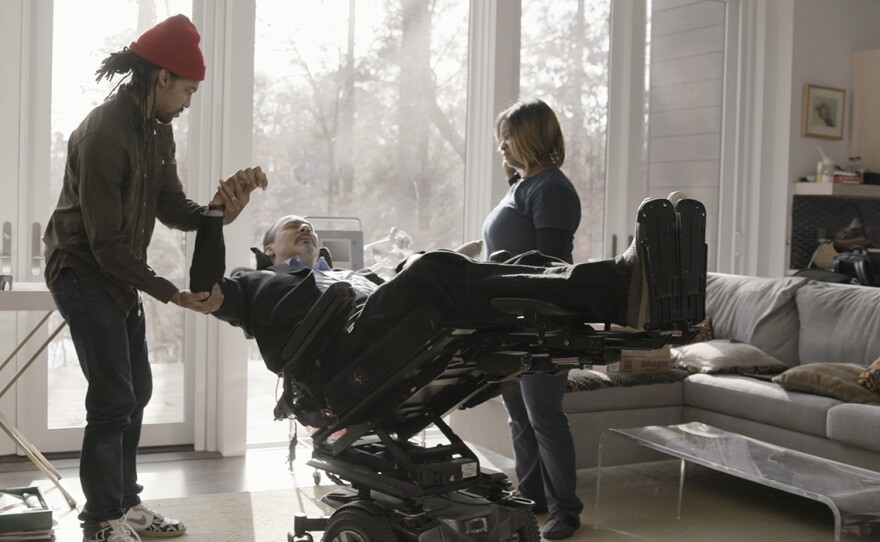 Phil Freelon stretches his limbs, with assistance of son Pierce Freelon and nursing assistant Helah Smith, at his home in Durham, N.C.