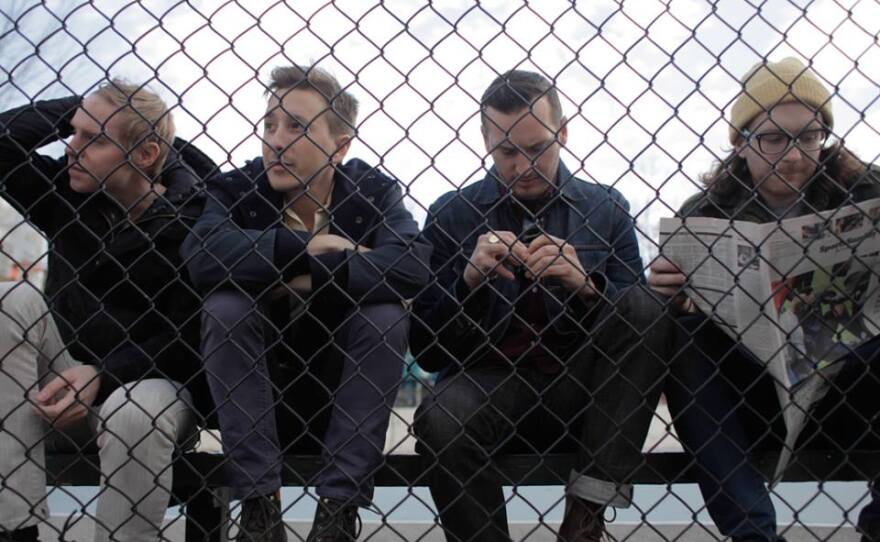 Members of indie-rock band Bear Hands sitting behind a fence, 2014. 