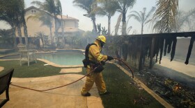 A firefighter puts water on a house fence during a wildfire in Carlsbad, May 14, 2014.