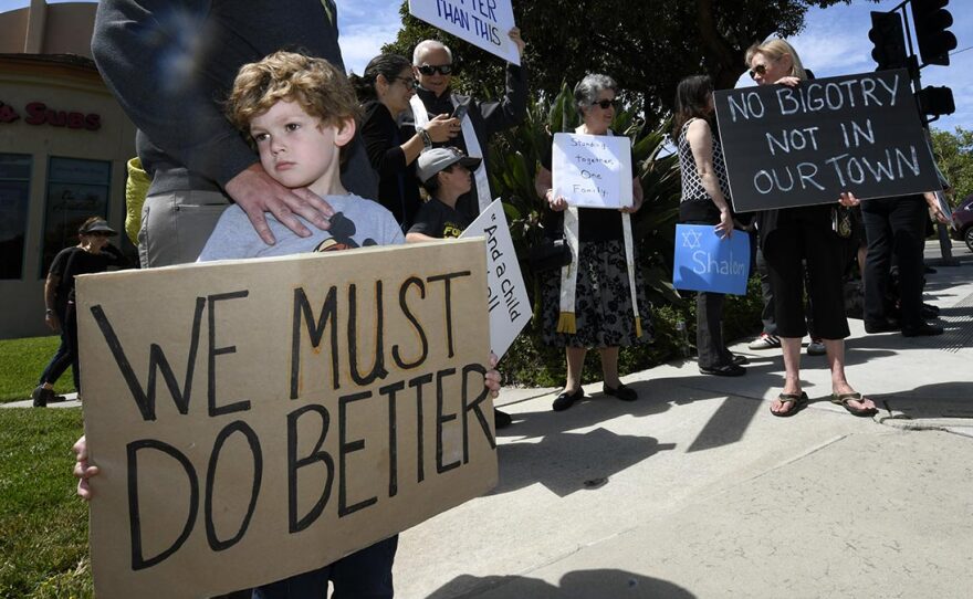 Kyle Fox, 4, and his father Brady Fox hold a sign at a Sunday vigil held to support the Chabad of Poway synagogue. A teenager opened fire at the synagogue near San Diego on Saturday, killing one and injuring three others.