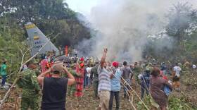 People stand around a military cargo plane that crashed after taking off from Puerto Leguizamo, Colombia, a remote municipality in the Amazonian province of Putumayo, Monday, March 23, 2026.