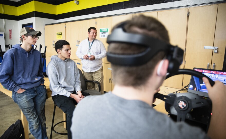 Tucker Bubacz, Peter Vilas Novas, and instructor Eric Young look on as Joshua Hewitt practices navigating intersections on a simulator, a big component of their training before they get their permits.