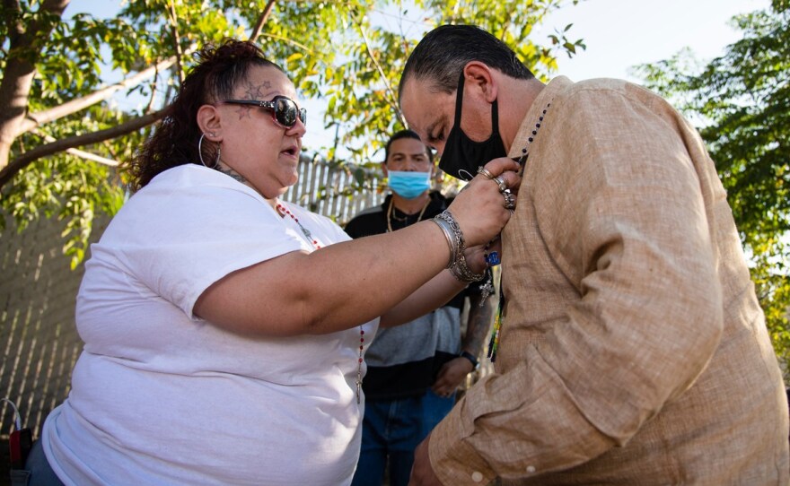 Mandy Sanchez, left, places a rosary around Sammy Nunez, right, at the Brandon Harrison Memorial Garden in Stockton, Calif. on September 23, 2020. Sanchez is the mother of Adrien Sancez who has a tree in the garden.