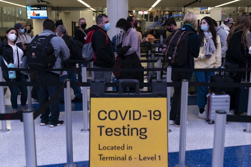Travelers wait in line for screening near a sign for a COVID-19 testing site at the Los Angeles International Airport in Los Angeles, Wednesday, Nov. 24, 2021.