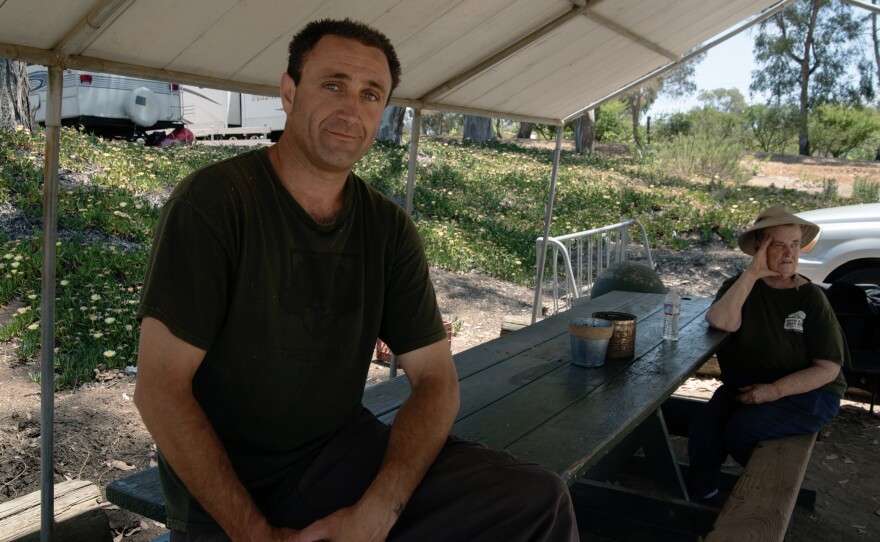 Travis Morris sits in the shade with other employees of Green Oaks Ranch on June 10, 2024, in Vista, Calif. He is in the men's addiction recovery program, where participants help maintain the property's landscaping, do maintenance work, and provide services to the people staying at the retreat.