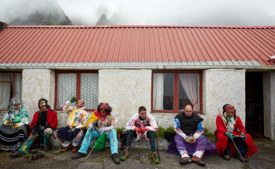 A group of Okalolies — Calvin Green (from left), Dean Repetto, Christopher Swain, Shane Green, Kieran Glass, Cedric Swain and Callum Green — take a break from roaming around the village. Roaming normally lasts a few hours, and the men will stop for breaks at friendly houses to cool off before putting their masks back on.