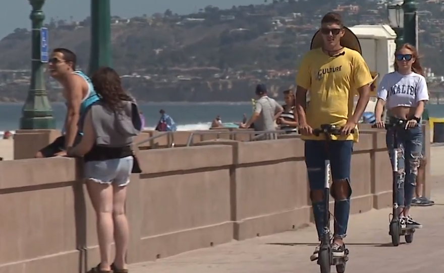 People ride electric scooters on the Mission Beach boardwalk, July 3, 2018.