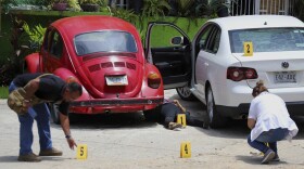 Forensics place numbers by evidence near the body of a woman who was found dead between two cars parked outside a restaurant in Acapulco, Mexico, Sunday, July 22, 2018.