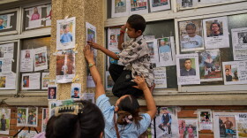 A young boy is helped by a women to put up a photograph of her missing relative on a wall alongside photographs of missing and deceased people displayed outside a government hospital in Kathmandu, Nepal, Sunday, Aug. 30, 2026.