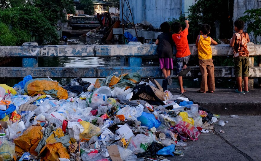 A pile of plastic waste and other garbage next to children playing on a bridge in the Philippines.