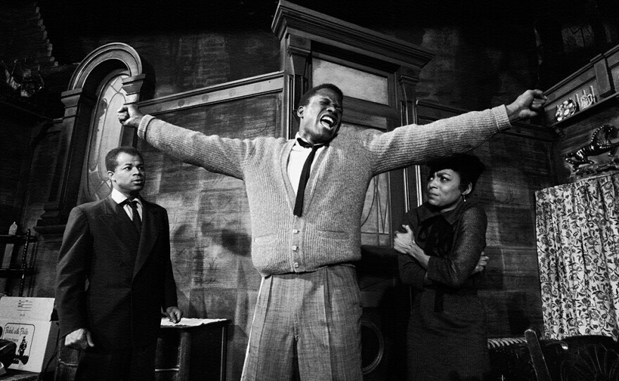 Sidney Poitier stands with arms outstretched in a dramatic scene from the play <em>A Raisin in the Sun</em>, with actor Ruby Dee visible on the right.