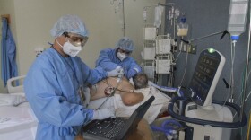 In this May 14, 2020 photo, Dr. Damian Gutierrez, left, and Dr. Miguel Vazquez, left, assess the lungs of a new coronavirus patient, in Tijuana, Mexico. Tijuana hospitals have become swamped with suspected COVID-19 patients. 