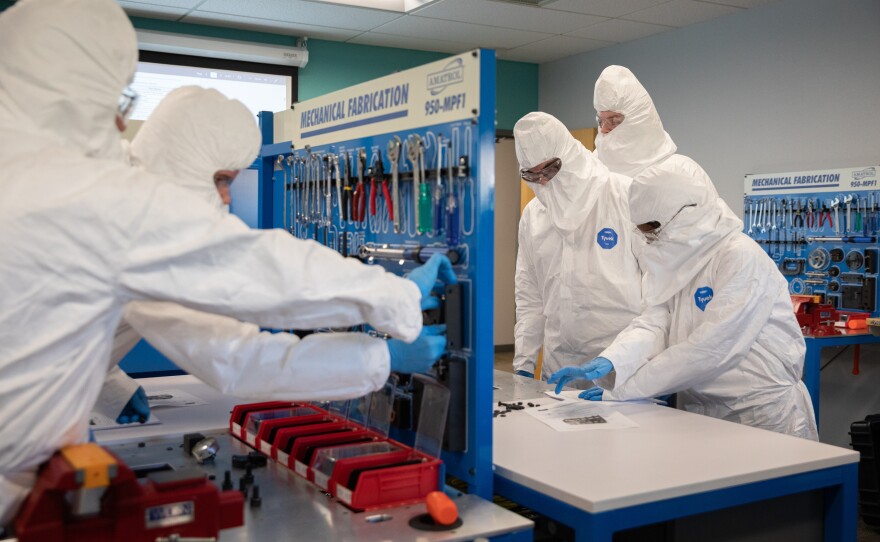 Students work in teams, handling washers, wrenches and bolts while dressed in the kind of gear worn inside clean rooms in semiconductor plants.