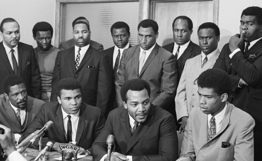 In this 1967 photo, black athletes gather for a meeting to hear Ali's view on rejecting Army induction. The photo shows: (front row) Bill Russell; Ali; Jim Brown and Lew Alcindor. Back row (left to right): Carl Stokes (Democratic state representative), Walter Beach, Bobby Mitchell, Sid Williams, Curtis McClinton, Willie Davis, Jim Shorter and John Wooten.
