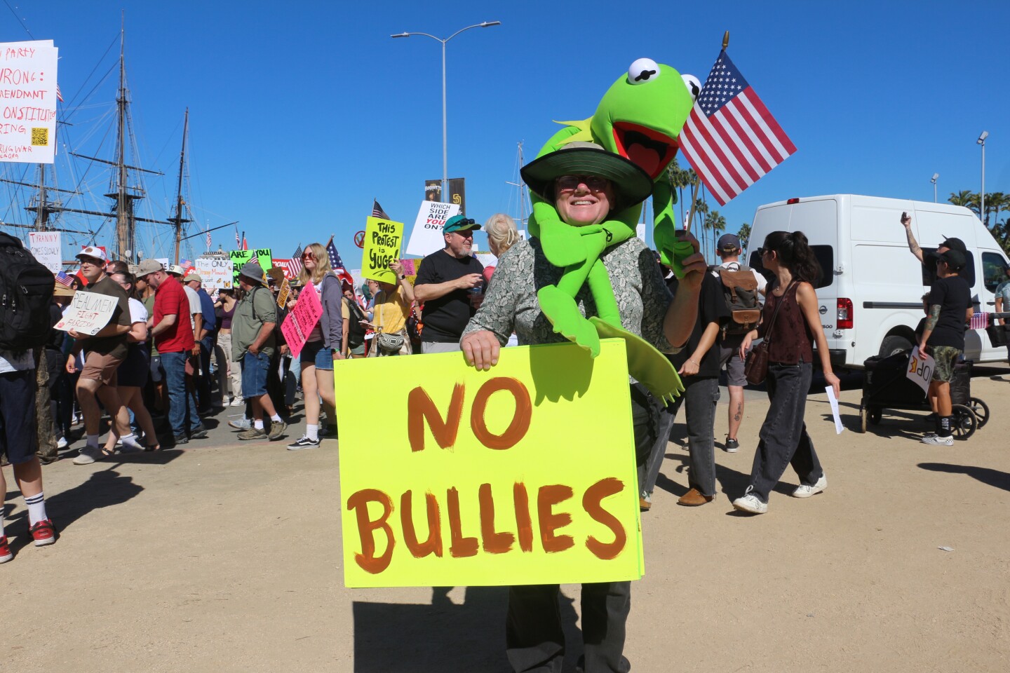 Mary Decker is wrapped with a Kermit the Frog plush toy and holds a sign that reads "No Bullies" during the "No Kings" protest rally at Waterfront Park on Oct. 18, 2025.