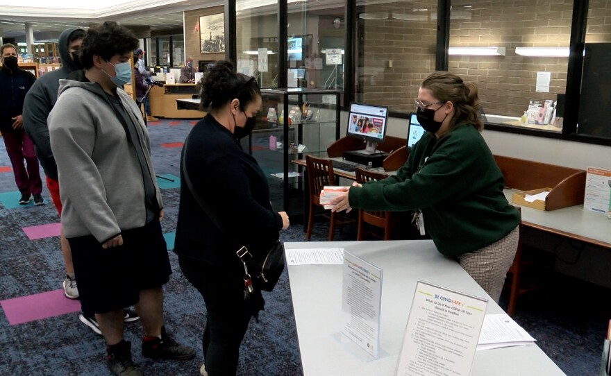 A woman waits inside the county's El Cajon branch library and is handed a free rapid COVID-19 test kit.