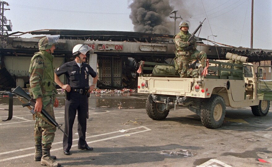 National Guardsmen and a police officer take up security positions in front of a burned and looted shopping center, May 1, 1992, in central Los Angeles.