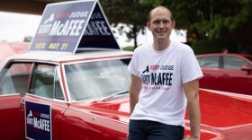 Fulton Superior Court Judge Scott McAfee leans against a 1965 Cadillac Fleetwood that has been in his family for years, while campaigning at a parade in Atlanta on April 27. McAfee, the trial judge in the Georgia election interference case, is up for reelection this month in a nonpartisan race.