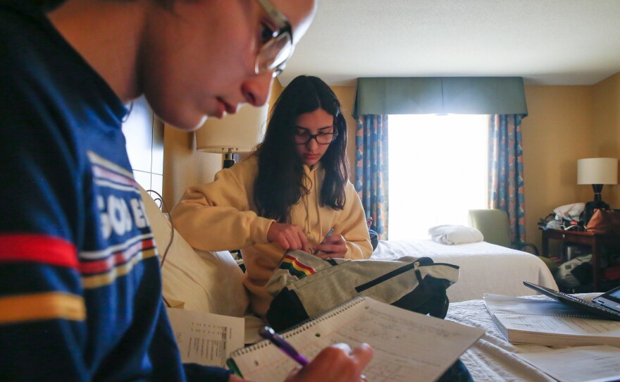 The Roldán sisters do their homework on the bed in the hotel room they share with their mom and stepdad.