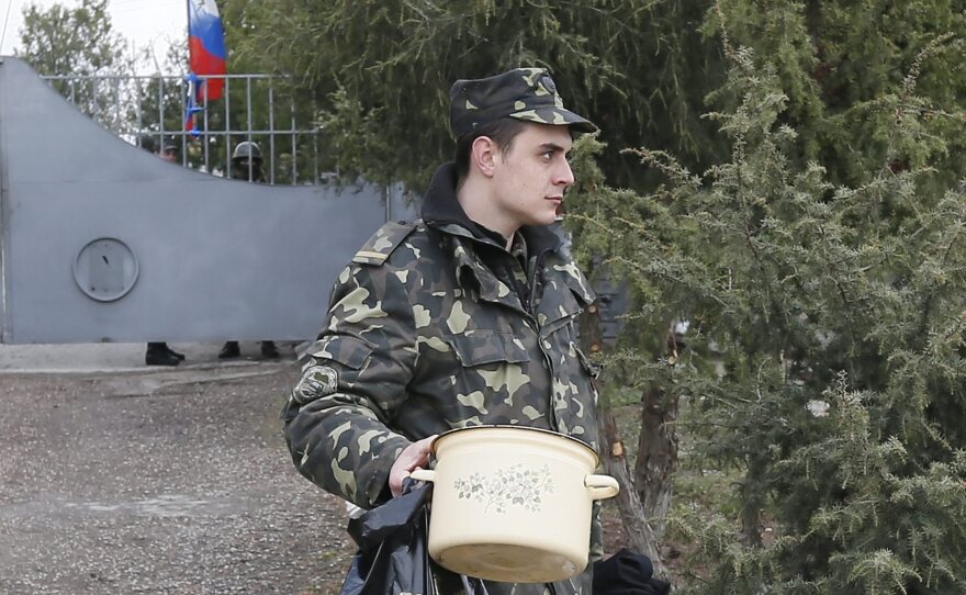 A Russian flag flies behind him Thursday as a Ukrainian soldier leaves what was one of his military's bases outside Simferopol, on the Crimean Peninsula. Local "self-defense forces," followed by Russian troops, have seized many strategic locations.