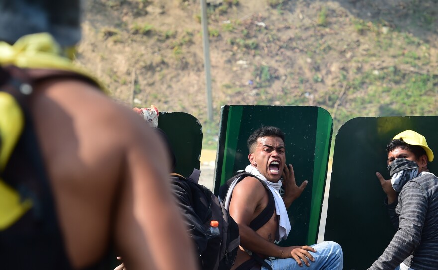 Opposition activists take cover behind advertisement placards during a fight with police in Caracas on Wednesday. More than two dozen people have died since protests against Venezuelan President Nicolas Maduro began to swell roughly a month ago.