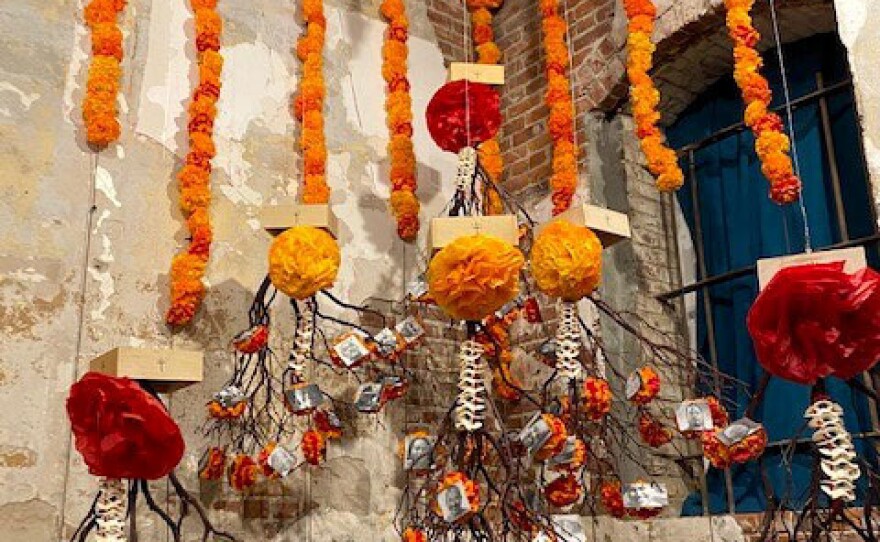 In her ofrenda,<em> </em><em>The Roots of Our Resistance, </em>Consuelo Flores pins photographs of first responders lost in the COVID-19 pandemic to marigolds that evoke 3D models of the virus.
