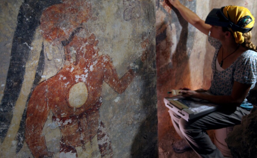 Conservator Angelyn Bass cleans and stabilizes the surface of a wall of a Mayan house that dates to the ninth century. The figure of a man who may have been the town scribe appears on the wall to her left.