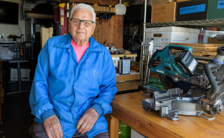John Gerardi, 90, sits at his work bench on Feb. 28, 2026. Gerardi has been attending a monthly local death cafe for almost a year. He said the conversations help ease loneliness after his wife passed away.
