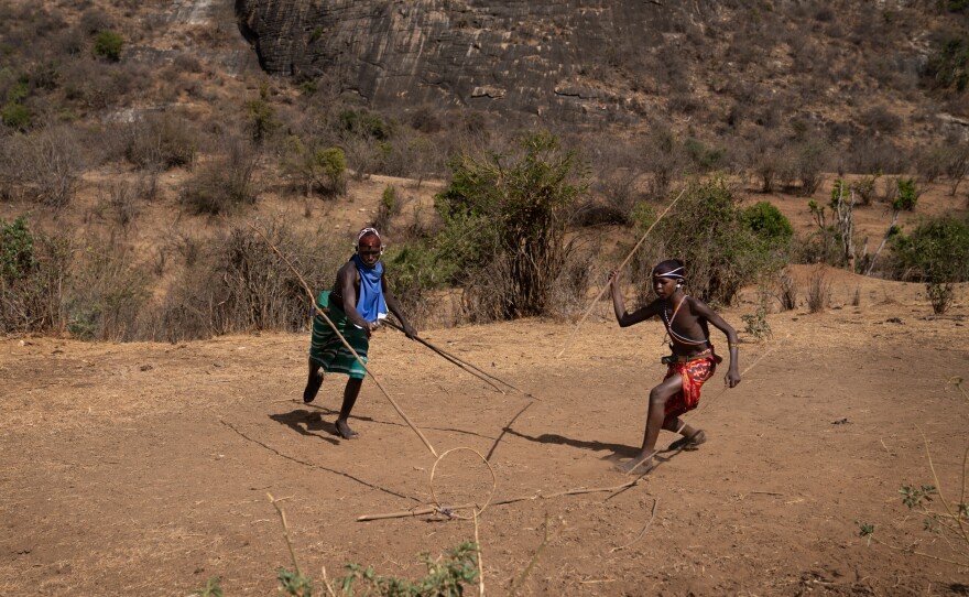 In the afternoon, when the work is done, the boys entertain themselves with an ancient game — throwing spears through a rolling hoop.