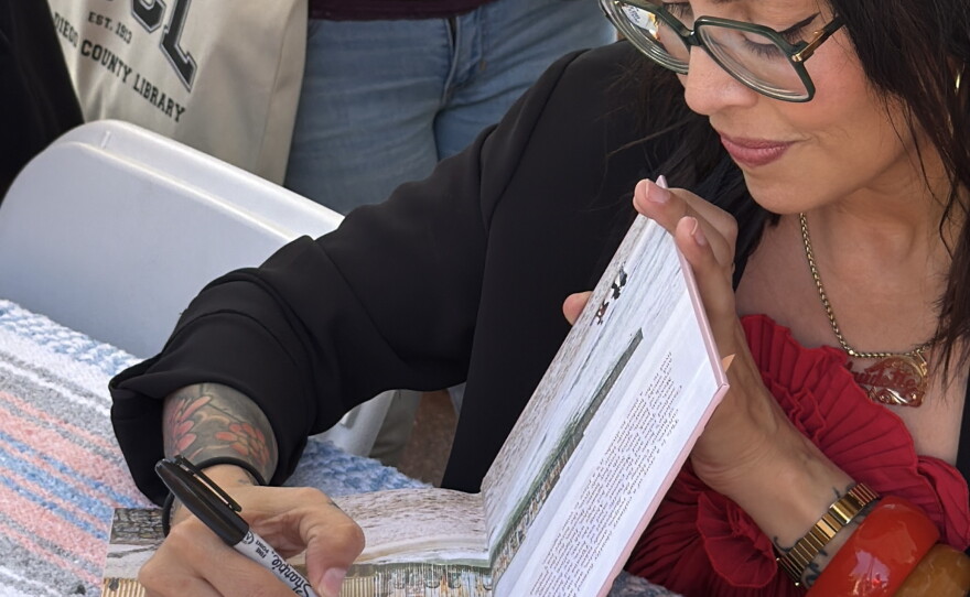 Chef and author Claudette Zepeda signs a copy of her cookbook, "Cooking the Borderlands: Spice and Smoke Between Mexico and the States," during the 2026 KPBS San Diego Book Festival at the University of San Diego on Aug. 22, 2026.