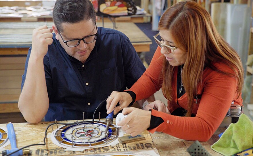 Head artist Debora Zalazare (right) helps show host Jorge Meraz (left) how to solder stained glass windows at Holdman Studios South in Ensenada, Baja Calif.