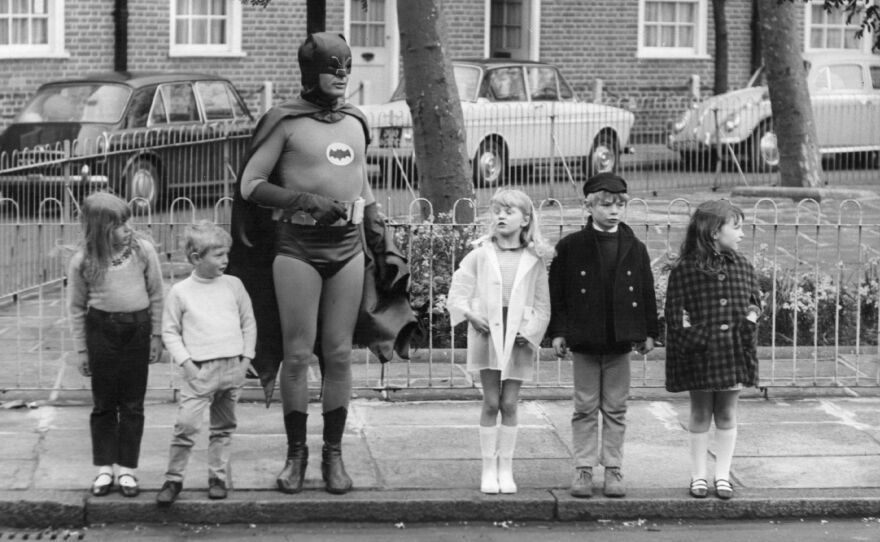 "What Batman provides, what all superheroes provide is this notion that good will triumph over evil," says author Glen Weldon. "That evil will have its day, but there will be somebody up there who will keep trying, who will keep looking out for us. ... He's catharsis in a cape." Above, Adam West, as Batman, makes a road safety film with child actors in Kensington, London in the late 1960s.