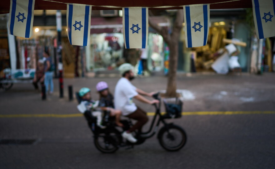 Israeli flags hang at a shop as a bicyclist carrying children passes by, Wednesday, Oct. 28, 2026, in Tel Aviv, Israel, the day after Israel's general election.