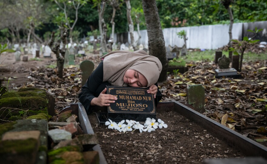 Anis Khuprotin, 28, rests her head on the gravesite of her husband, Muhamad Nur, in Tegal, Indonesia, on June 13, 2025. Anis' husband died on board a commercial fishing vessel after a piece of equipment came loose and struck him in the head. Staff from the recruiting agency the hired her husband told her he died of a heart attack instead of admitting the truth in an attempt to avoid paying insurance fees to the family.