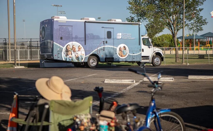 A resident sits on a chair in front of the Saint Agnes Mobile Health Unit mobile clinic parked in the parking lot of Rojas Pierce Park in Mendota on Aug. 28, 2025.