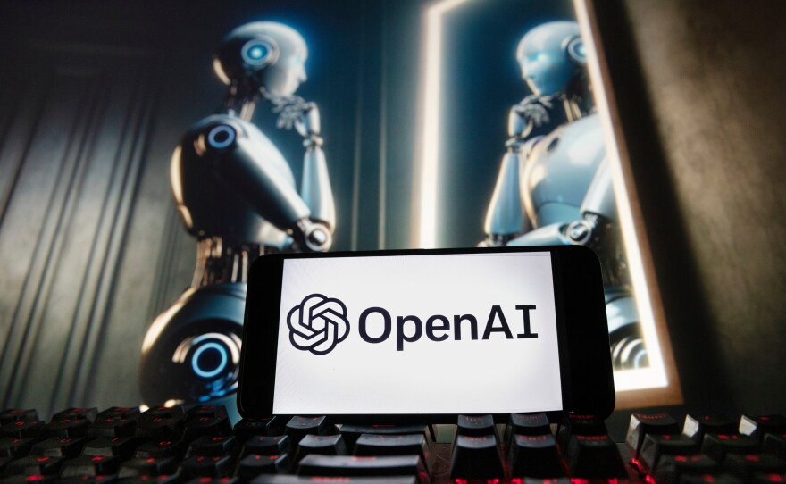 FILE - The OpenAI logo is displayed on a cellphone with an image on a computer monitor generated by ChatGPT's Dall-E text-to-image model, Dec. 8, 2023, in Boston.