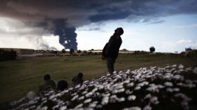 Libyan rebels watch as pillars of smoke rise from the oil facility just outside the town of Ras Lanuf on Wednesday.