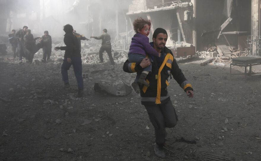 A Syrian man carries a child injured in the government bombing of eastern Ghouta, on the outskirts of Damascus on Monday.