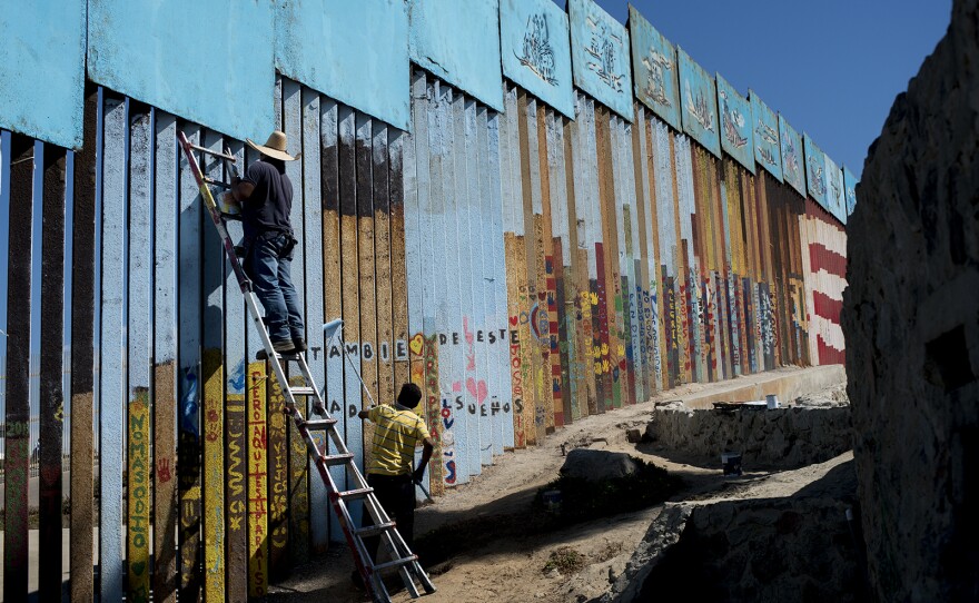 Enrique Chiu stands on a ladder to paint the U.S.-Mexico border fencing at Friendship Park in Tijuana on Oct. 7, 2017.