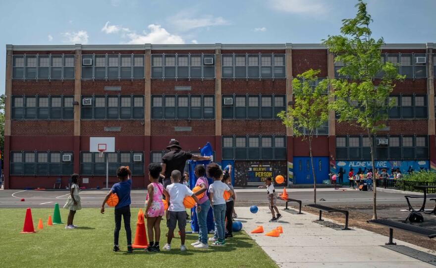 Gym teacher Delane Hart-Johnson leads kids through an exercise on Fun Day at the Add B. Anderson School. The renovated schoolyard includes a swath of green turf, benches for students to sit on and landscaped trees.