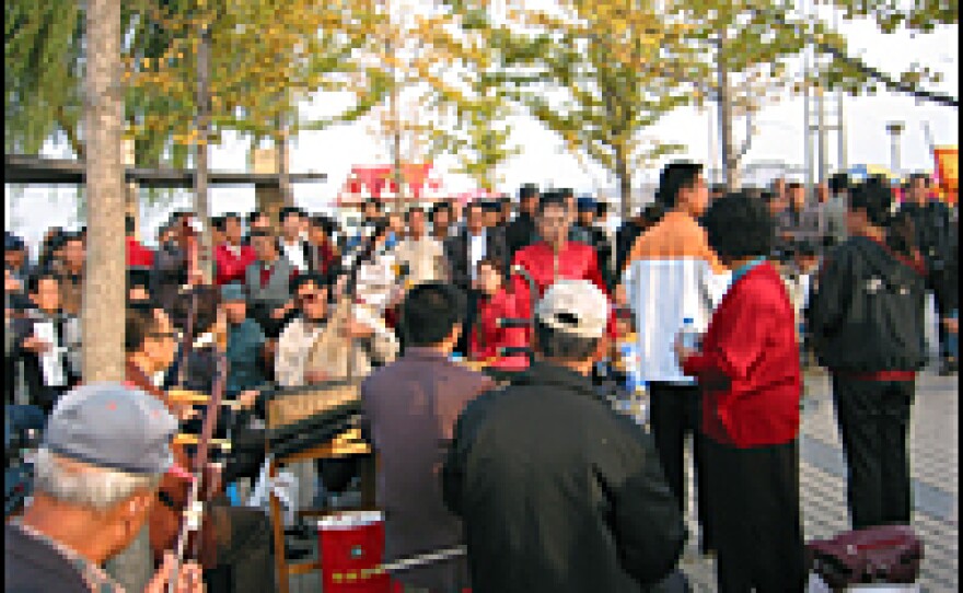 Residents hold an impromptu folk music performance in a riverside park in Dandong, China. The smokeless smokestacks of Sinuiju are visible from the waterfront.